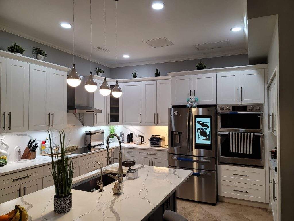 Modern kitchen with four pendant lights, high-tech stainless steel appliances, an island, a coffee station, high ceiling cabinets with under-cabinet lights, a hot top stove, and a wall oven.